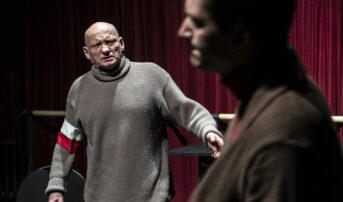 Kliknij by powiększyć zdjęcie. Alternatywny opis zdjęcia: Mężczyzna z biało-czerwoną opaską na ramieniu spogląda na drugiego mężczyznę.