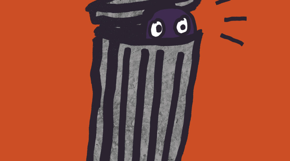 Plakat w pomarańczowym kolorze z ilustracją kosza na śmieci, z którego wygląda para oczu. Nad nim napis „Antygona w Nowym Jorku”, Janusz Głowacki.