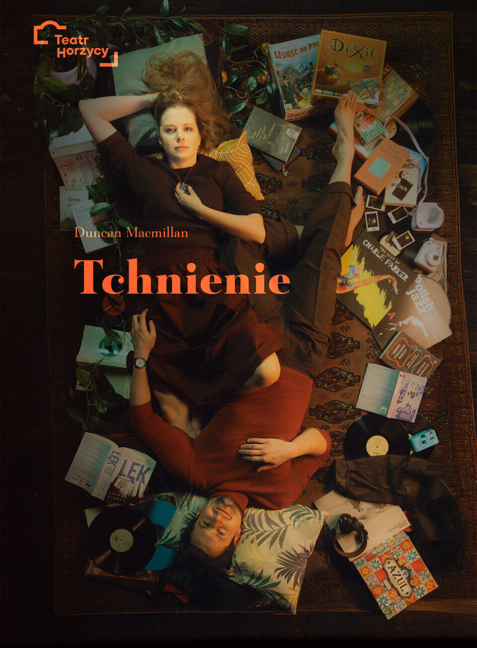 Plakat teatralny | Zdjęcie od góry. Dwie osoby leżą na dywanie, otoczone książkami, płytami winylowymi i różnymi przedmiotami. Wokół nich leżą gry planszowe, fotografie i inne drobiazgi. Na środku plakatu napis 