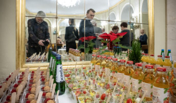 Stolik z przekąskami i napojami. Za stolikiem jest lustro w którym odbija się kilka osób w tym fotograf.