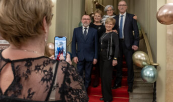 Kobieta robi zdjęcie grupie 5 osób, które stoją na schodach.