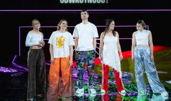 Kliknij by powiększyć zdjęcie. Alternatywny opis zdjęcia: Pięcioro aktorów stoi frontem na błyszczącej scenie. Pod ich stopami odbijają się kolory neonów i sylwetki. Nad zespołem pojawia się pytanie: „Czym jest odwrotność?”